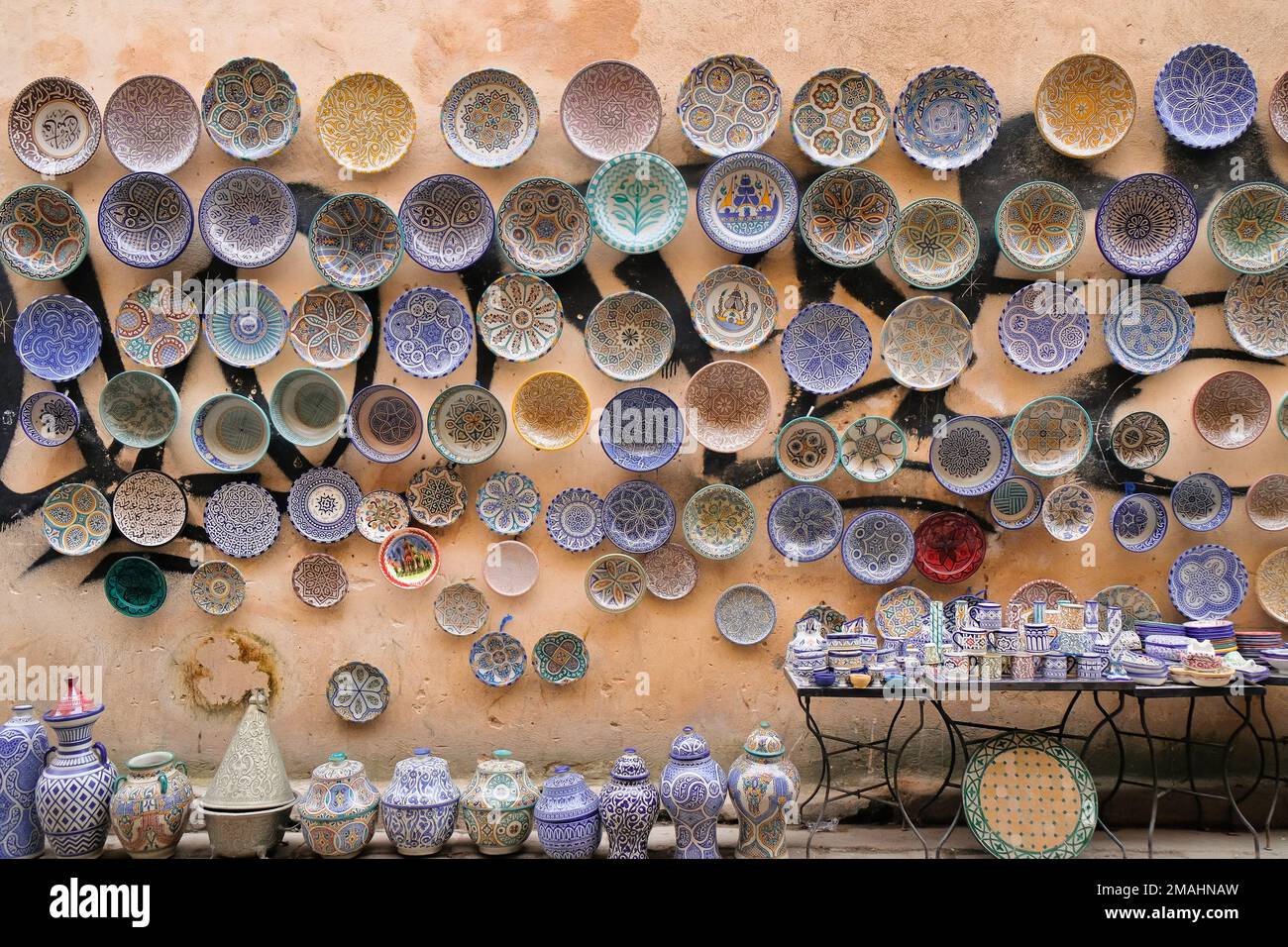 Fez, Morocco - ceramic goods for sale in Fes el Bali market. Cups and saucers on table, jars on floor, plates on vandalized wall. Travel background. Stock Photo