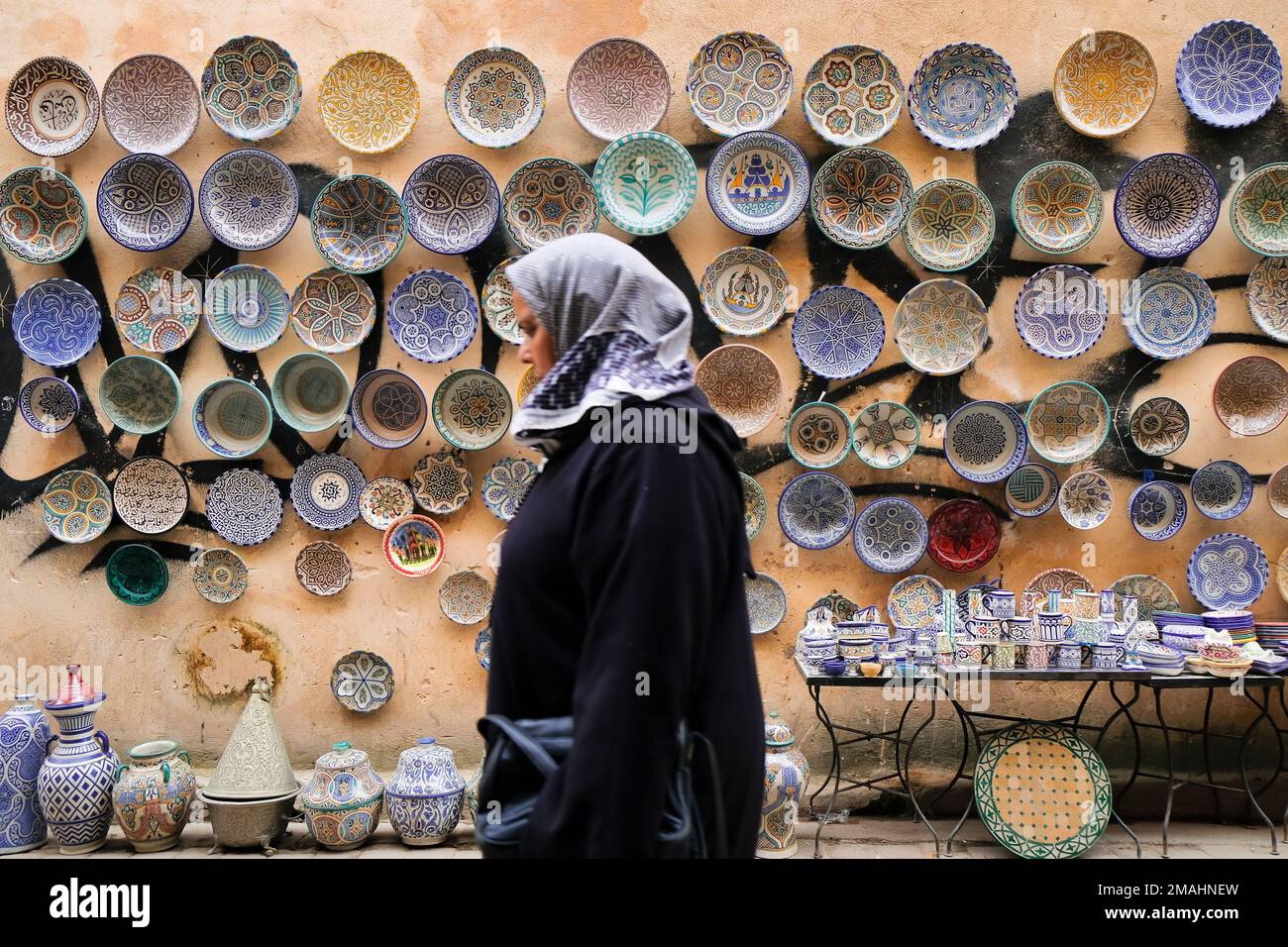 Fez, Morocco - blurry image of covered local muslim woman walking past ceramic goods for sale in Fes el Bali market. Horizontal Fes Travel background. Stock Photo