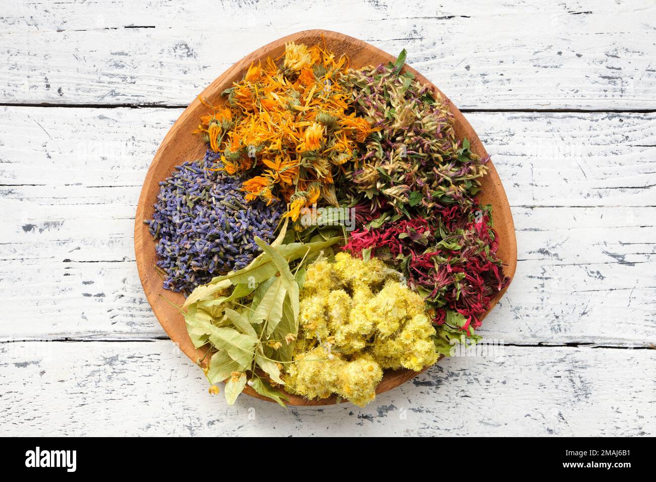Wooden plate of medicinal herbs - lavender, calendula, red clover, helichrysum, lime tree flowers - ingredients for making of herbal medicine drugs, t Stock Photo
