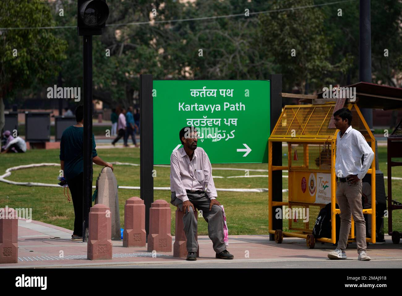 A man rests on a newly constructed pillar in front of a road signage ...