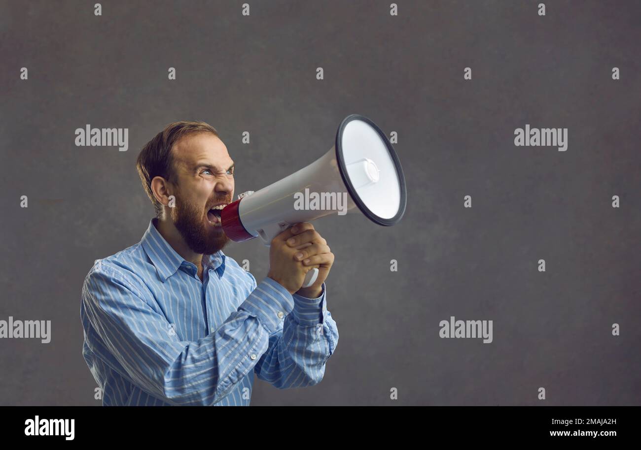 Bearded man in a blue shirt shouted loudly into a megaphone. Stock Photo