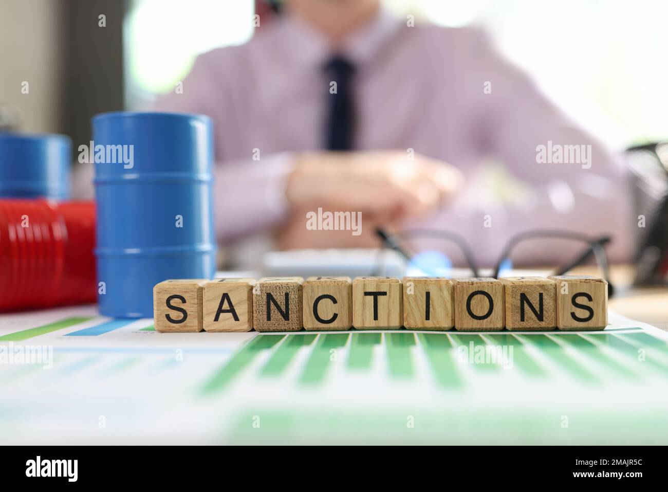 Word sanctions collected from cubes on financial reports, barrels of oil and manager in background. Stock Photo