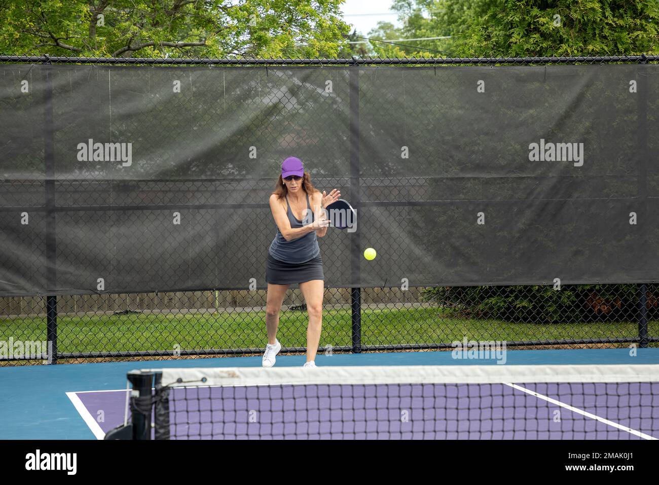 A pickleball players hits a serve on a suburban pickleball court during