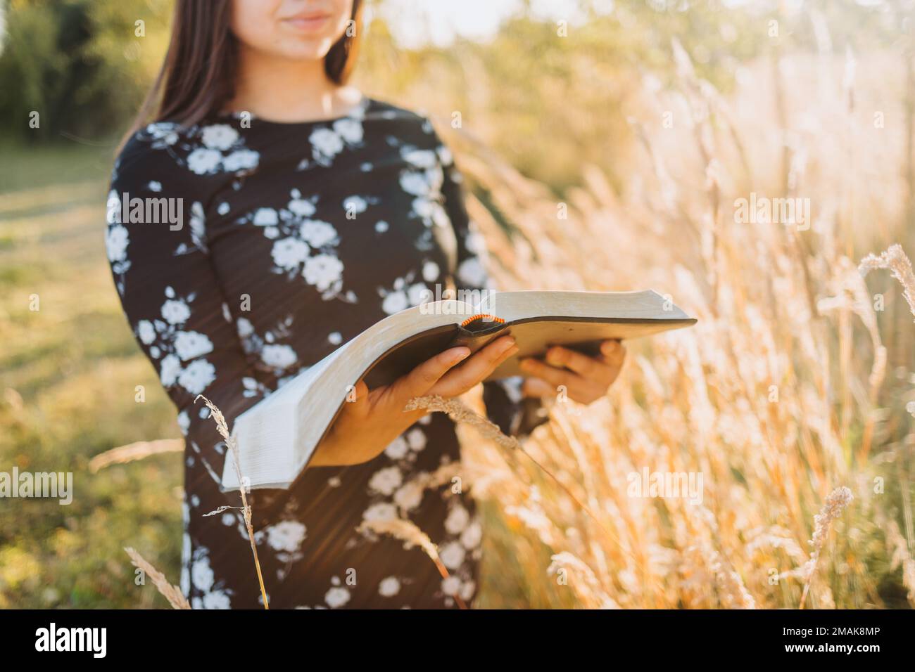 Young religious christian girl holding and reading her bible, outside