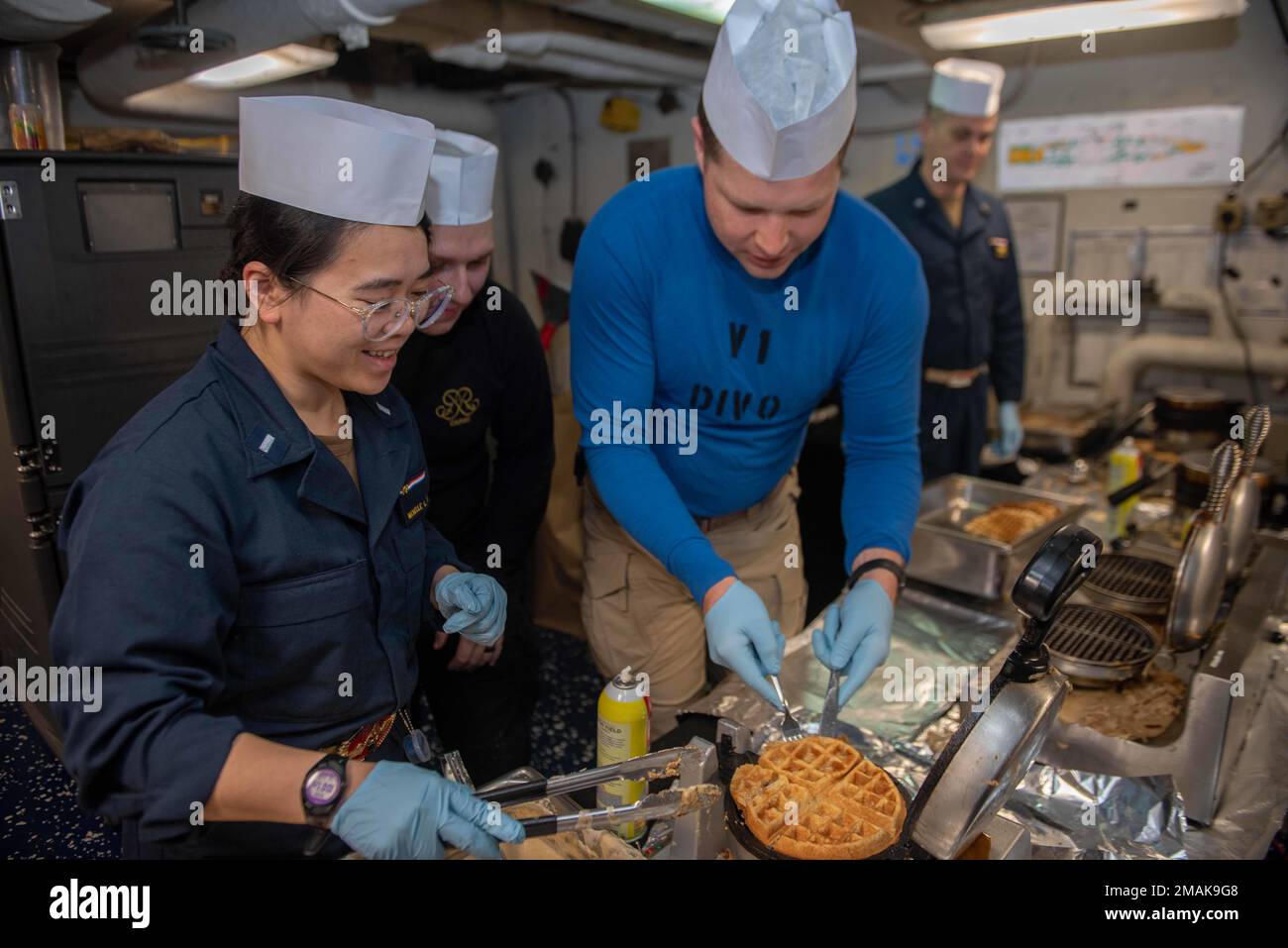 220529-N-UF592-1015 PHILIPPINE SEA (May 29, 2022 Lt. j.g. Michelle Tran, left, from Centreville, Virginia, and Lt. Thomas Whiting, from Baltimore, prepare waffles on the aft mess deck of the U.S. Navy’s only forward-deployed aircraft carrier, USS Ronald Reagan (CVN 76). Each Sunday at sea, supply department organizes shipboard volunteers to prepare and serve brunch to more than 5,000 personnel. Ronald Reagan, the flagship of Carrier Strike Group 5, provides a combat-ready force that protects and defends the United States, and supports alliances, partnerships and collective maritime interests i Stock Photo
