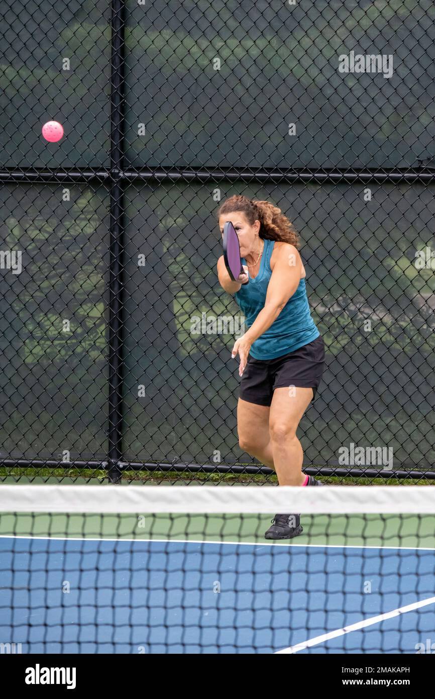 A pickleball player serves the ball on a suburban pickleball court