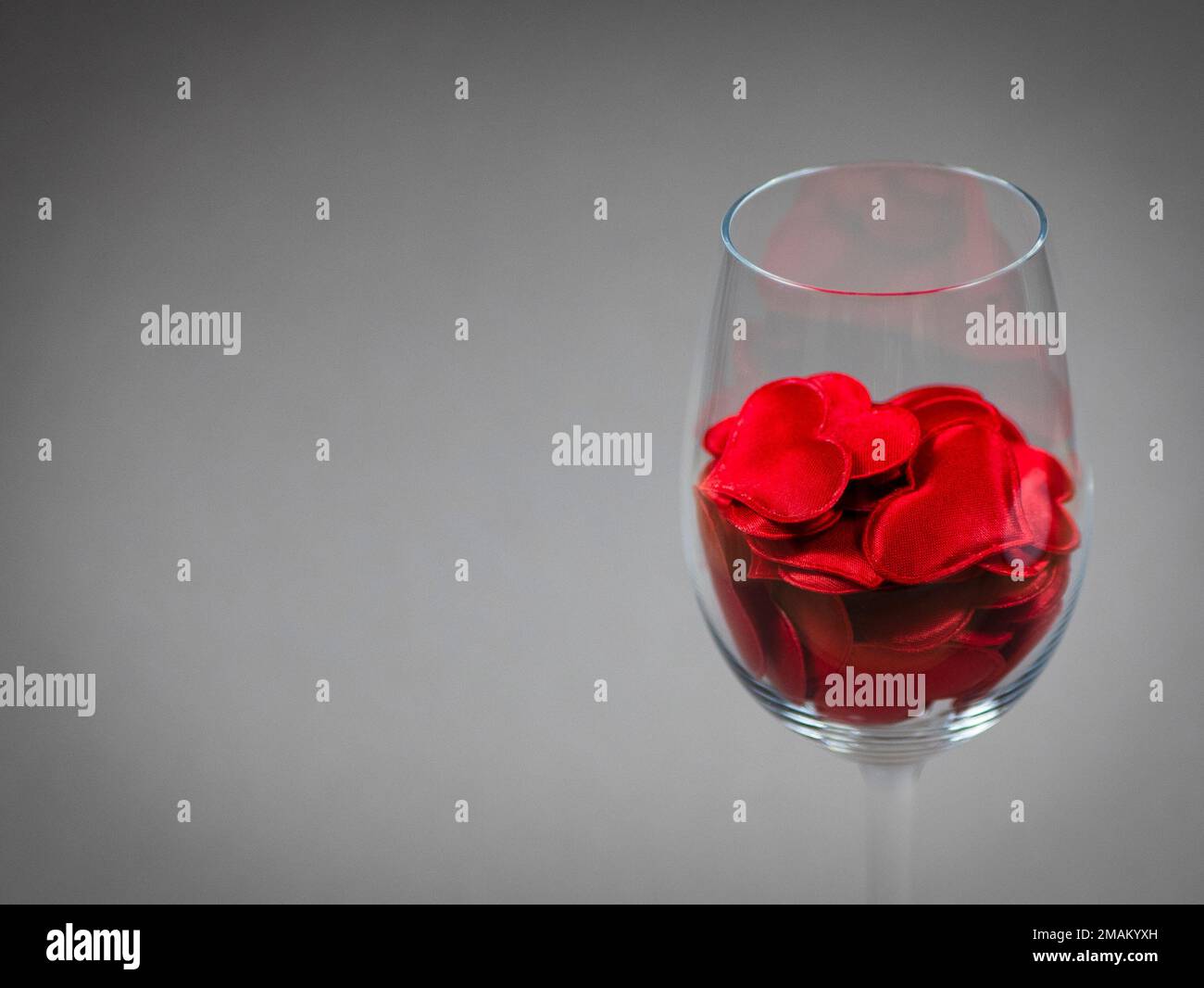 Wine glass filled with red hearts, copy space. Concept of the love