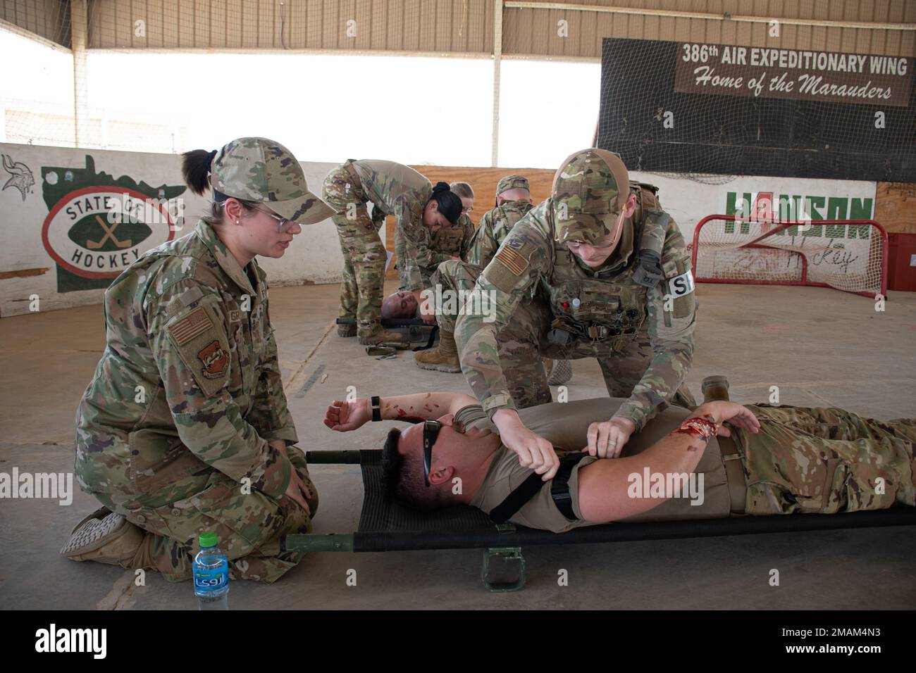 U.S. Air Force Staff Sgt. Elissa Gray, left, paramedic, 386th Expeditionary Medical Group, guides Senior Airman John Roach, security forces specialist, 387th Expeditionary Security Forces Squadron, on how to apply a tourniquet to control simulated massive bleeding on Staff Sgt. Matthew Depodesta, firefighter, 386th Expeditionary Civil Engineer Squadron, during the joint coalition Tactical Combat Casualty Care course at a skating rink at Ali Al Salem Air Base, Kuwait, May 29, 2022. In the TCCC course, which replaced the Self-Aid Buddy Care course, U.S. service members and coalition partners pra Stock Photo