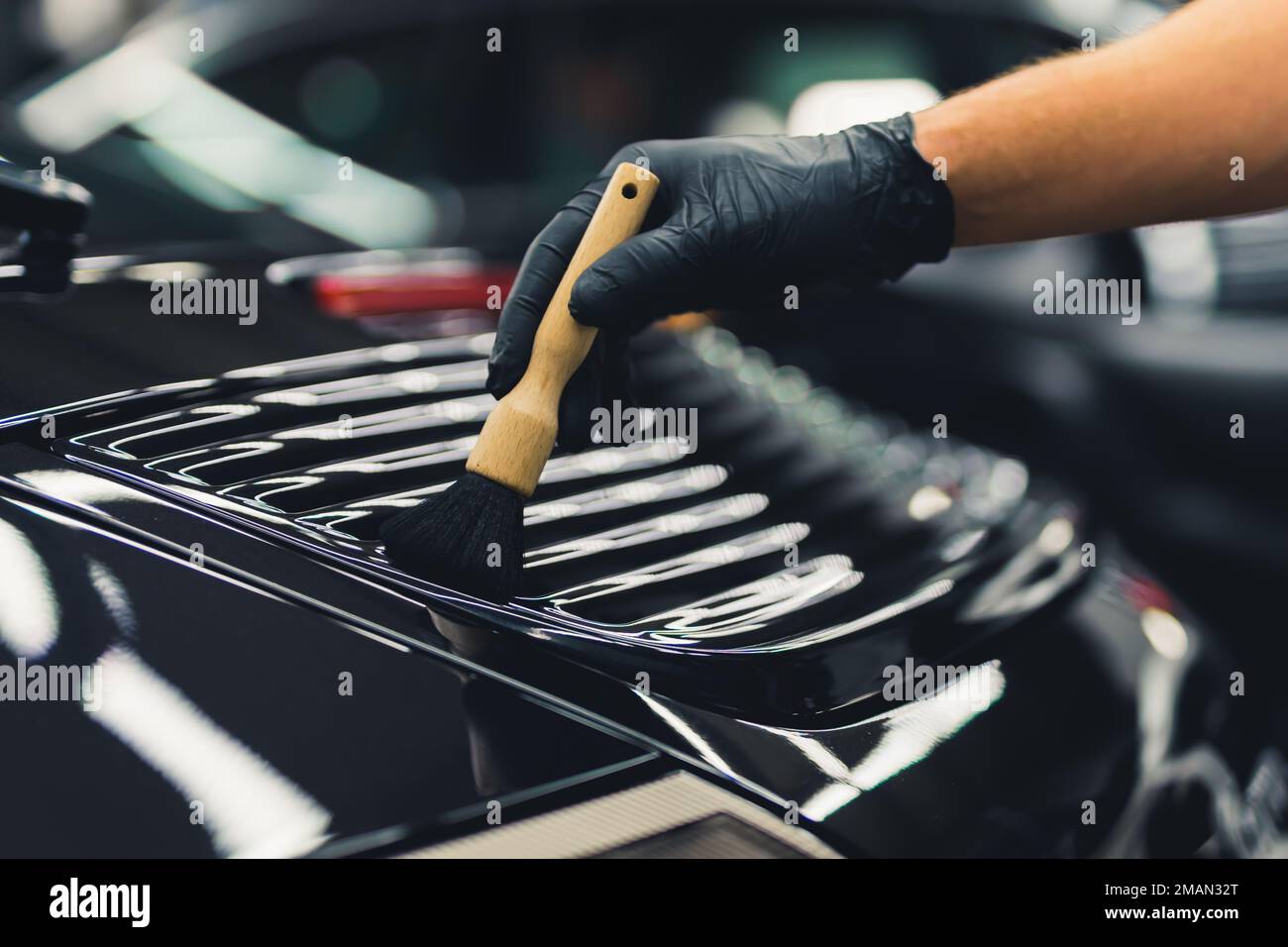 Luxurious sports car during car detailing. Unrecognizable man in protective gloves cleaning car spoiler with a brush. High quality photo Stock Photo