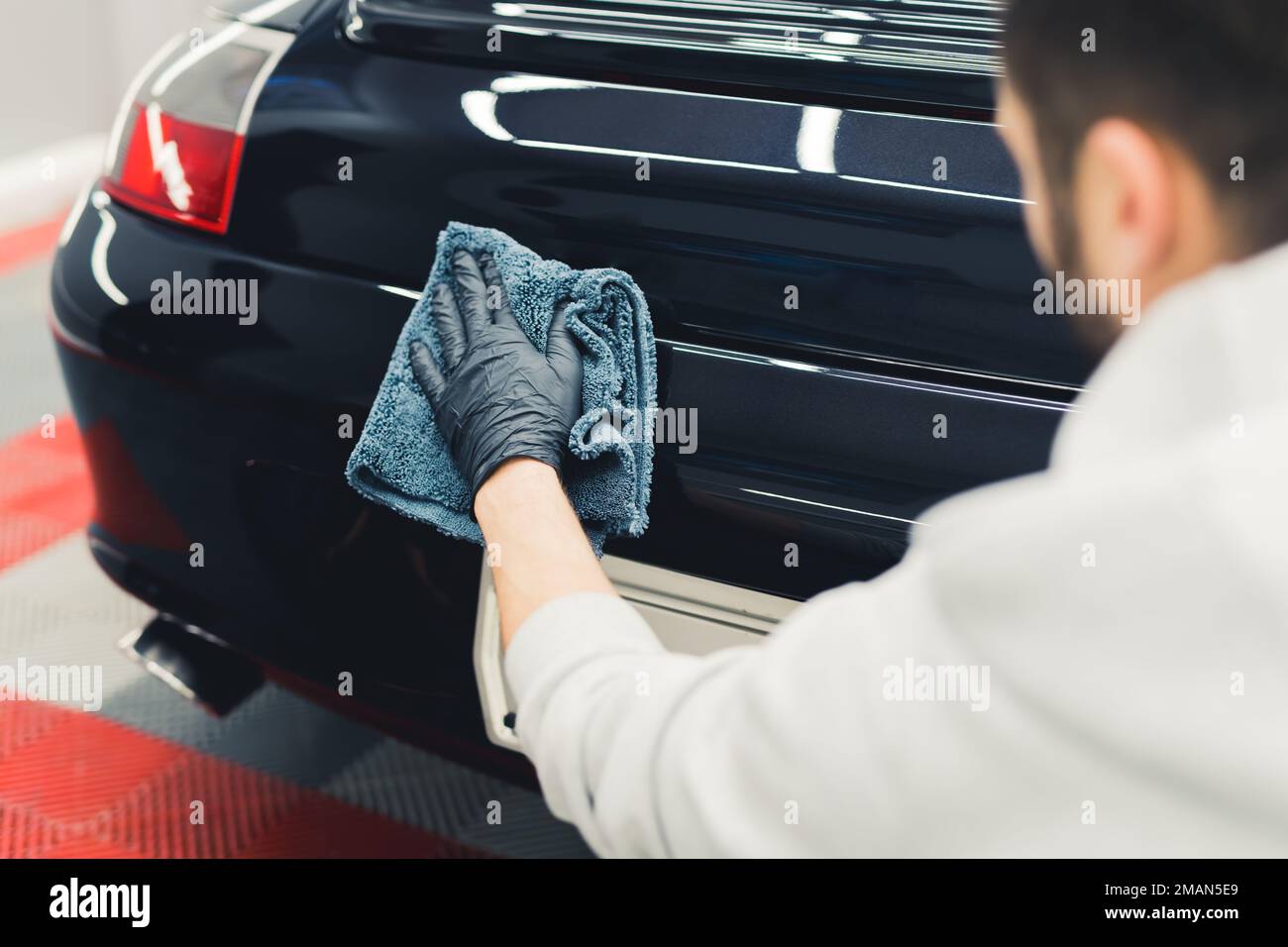 Back view of unrecognizable professional car detailer applying ceramic coating onto the back of luxurious black car. High quality photo Stock Photo