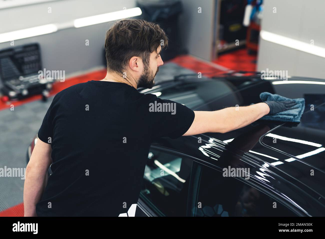 Male car service worker applying ceramic coating on a black sports car during car detailing. Top back view. High quality photo Stock Photo