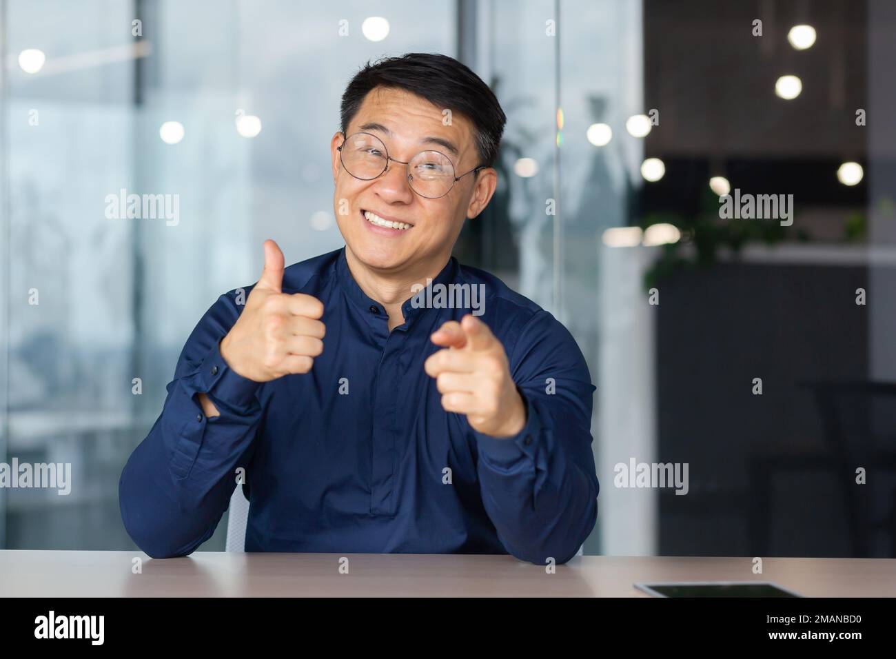 A successful Asian man inside the office is looking at the web camera, talking on a video call with colleagues, gesturing and smiling an online meeting with partners, talking to customers, pov Stock Photo
