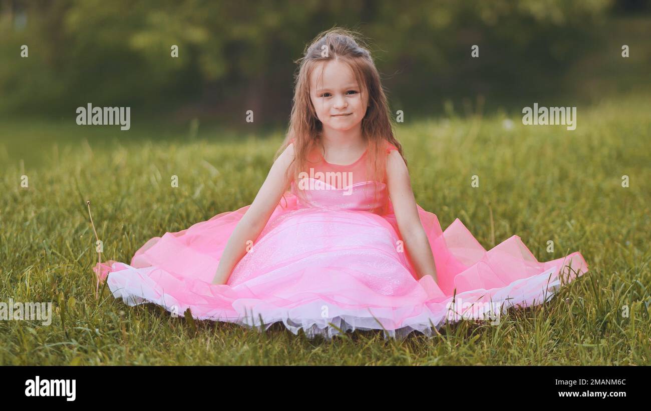 A little girl is sitting in a pink dress in the park Stock Photo - Alamy
