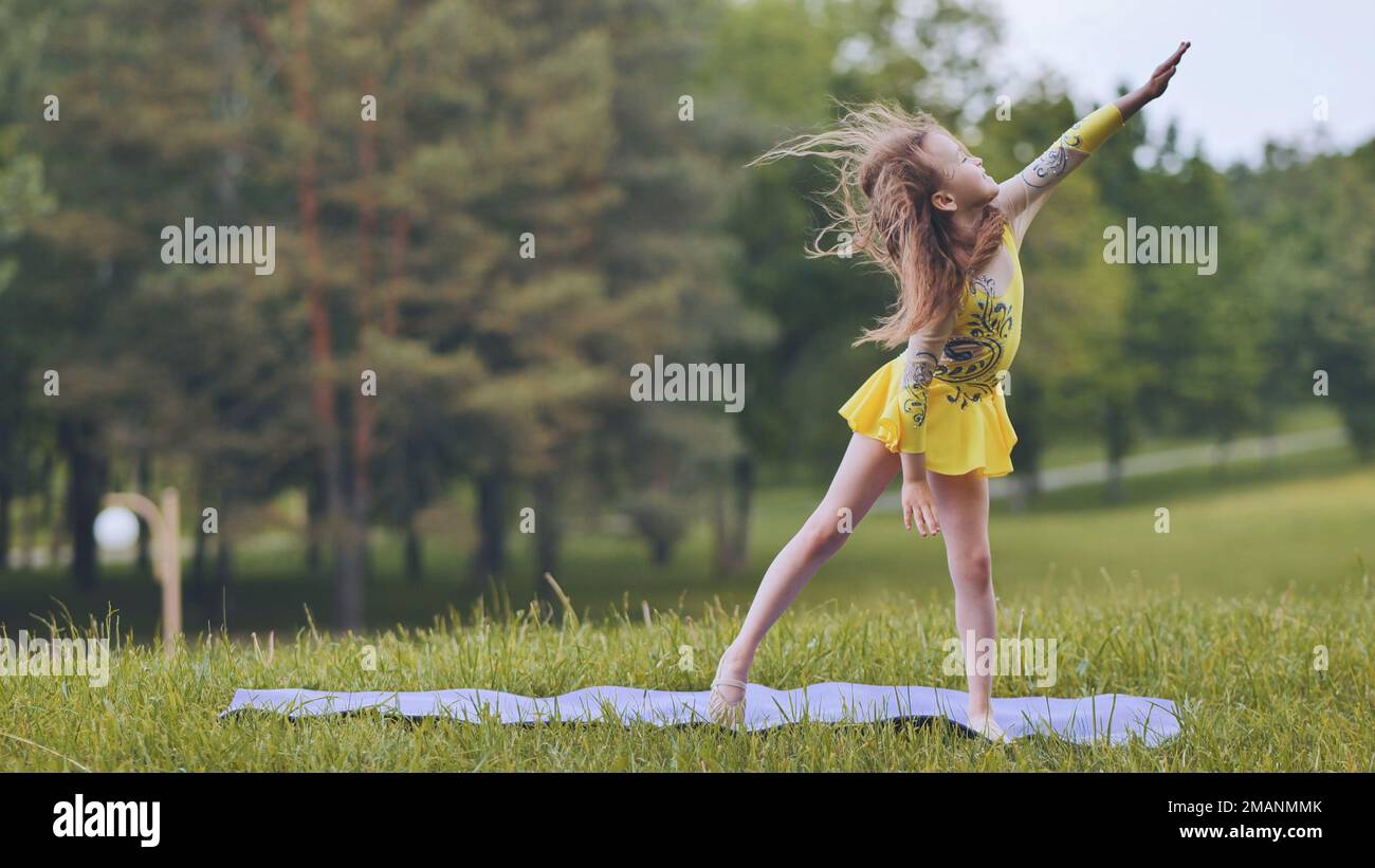 A little girl performs the elements of rhythmic gymnastics in the park