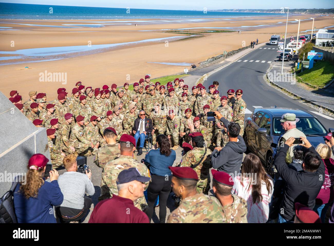Service members take a photo with WWII veteran, Charles Shay, on Omaha