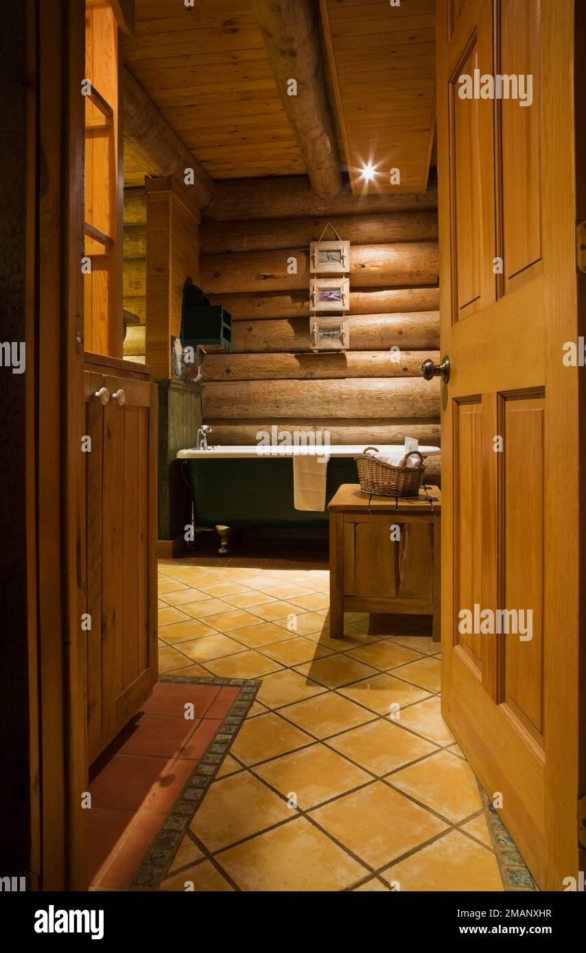 Freestanding roll top bathtub in main bathroom with ceramic tile floor inside Scandinavian style log home. Stock Photo