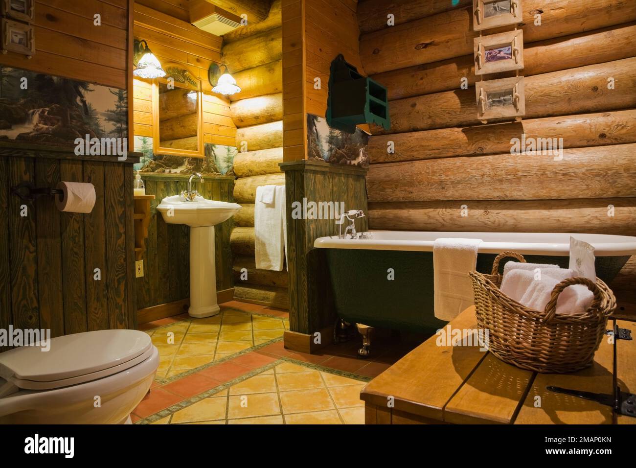 Toilet, pedestal sink and green freestanding roll top bathtub in main bathroom inside Scandinavian style log home. Stock Photo