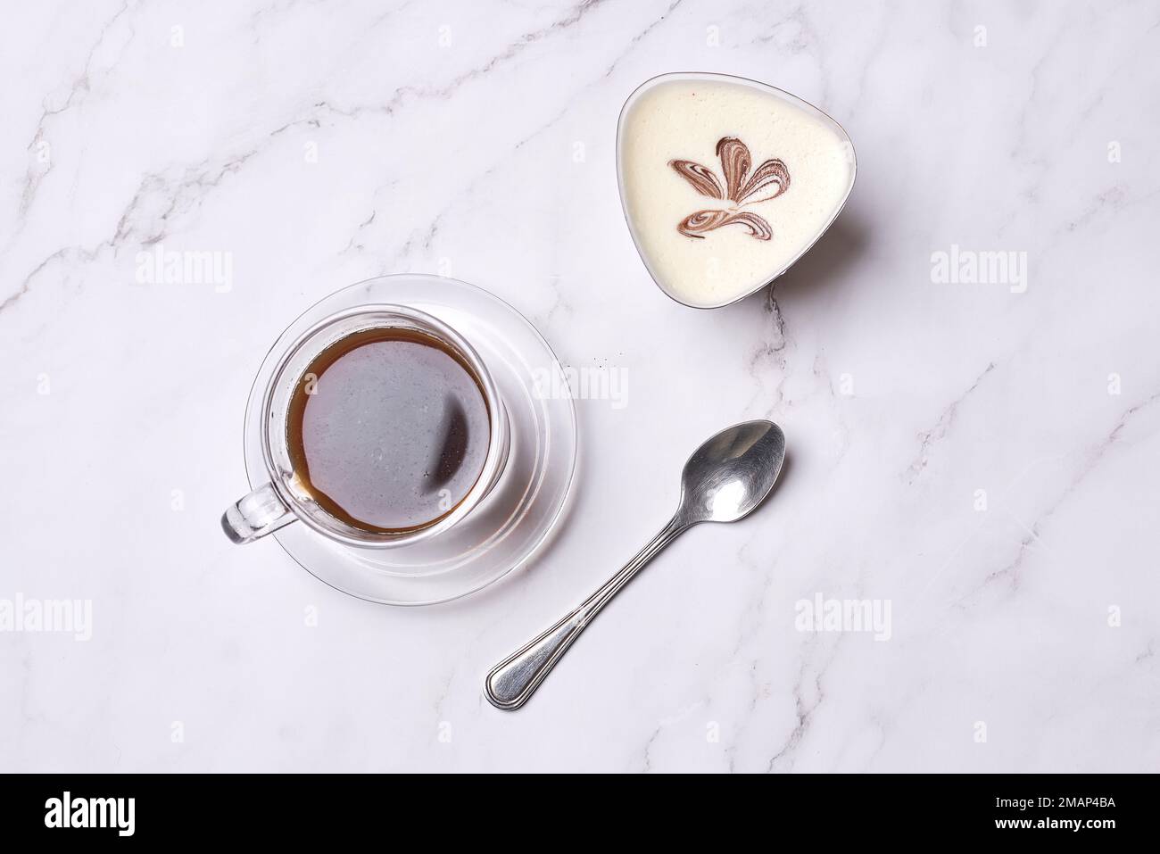a cup of coffee and spoon on a white marble table with a leaf drawn in the top right hand side Stock Photo