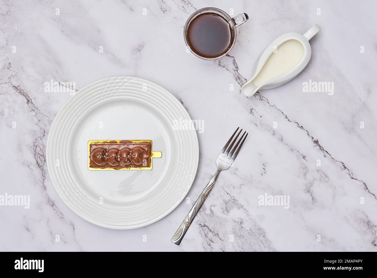 a piece of cake on a plate next to a cup of coffee and a spoon with chocolate frosting in it Stock Photo