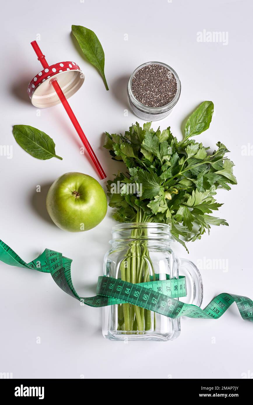 an apple, parise, and measuring tape on a white surface with green vegetables in the top right corner Stock Photo