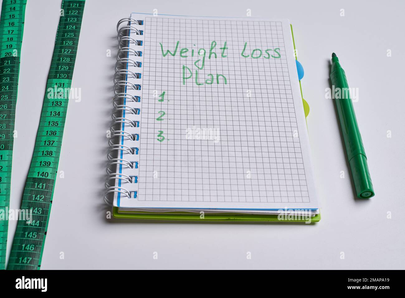 an open notebook with a green pen next to it and a measuring tape on the side. Weight loss plan Stock Photo