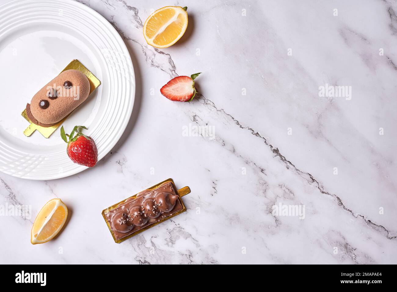 some desserts on a white plate with strawberries and lemon slices next to the plate is a piece of cake Stock Photo
