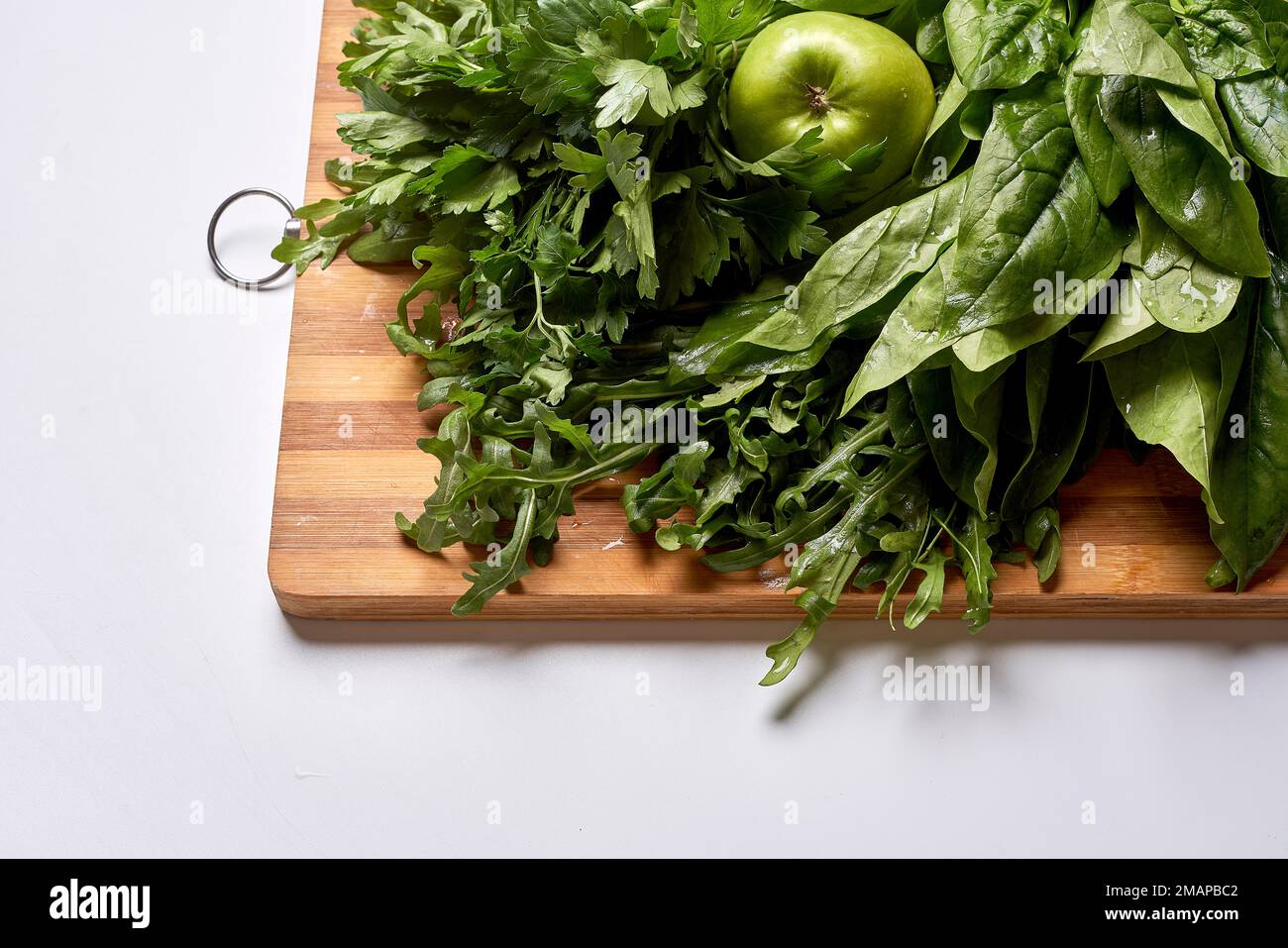 some greens on a cutting board with an apple in the top left and green leaves to the bottom right side Stock Photo