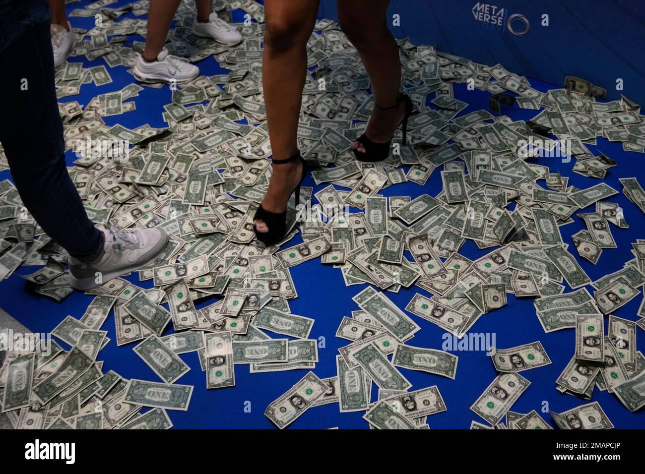 People walk on fake dollar bank notes at a cryptocurrency event in Madrid,  Spain, Saturday, Aug. 27, 2022. Spanish financial authorities are planning  to keep a close eye on a major cryptocurrency