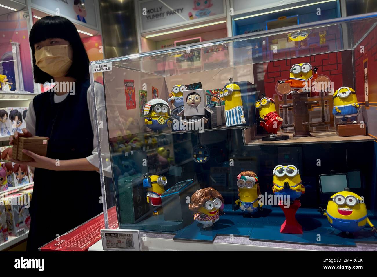 A woman wearing face mask walks by variety of Universal animation movie Minions toy figures on display for sale at the Chinese toy maker POP Mart store in Beijing, Tuesday, Aug