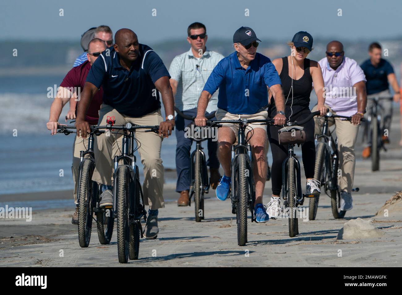 President Joe Biden rides a bicycle with others along the beach at
