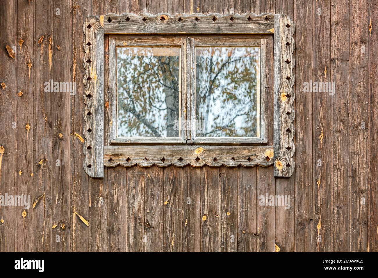 window with carved frame on weathered wooden wall of rural house Stock Photo