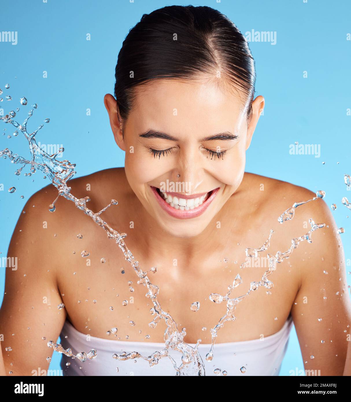 Face wash, skincare and woman isolated on blue background for beauty, cosmetics cleaning and happy. Smile of a person or model with water splash for Stock Photo