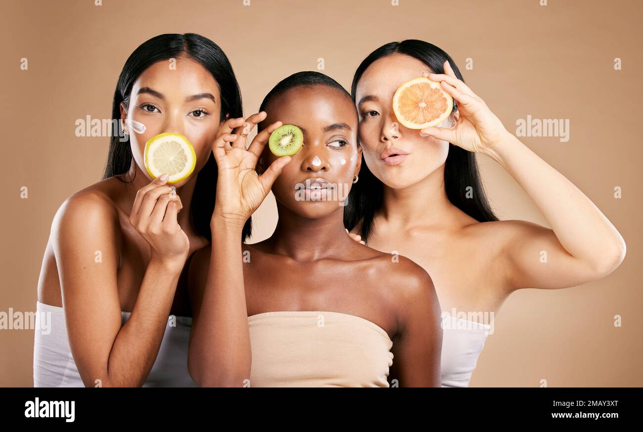 Skincare, diversity and women with fruit, cosmetics and dermatology with friends on brown studio background. Face, vitamin c or ladies with natural Stock Photo