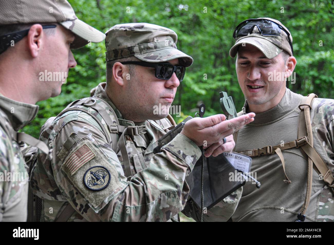 Staff Sgt. Richard Manley, combat arms instructor, uses a compass to determine an azimuth in the woods on Camp Dawson Army Training Site, near Kingwood, West Virginia, as fellow combat arms instructors Tech. Sgt. Jeremy Whitlow and Staff Sgt. Josh Huber observe. Two teams of defenders from the 445th Security Forces Squadron, Wright-Patterson Air Force Base, Ohio, raced to locate as many points as possible before time expired on June 7. In total, the Airmen traversed more than eight miles of rugged terrain during the all-day land navigation event Stock Photo