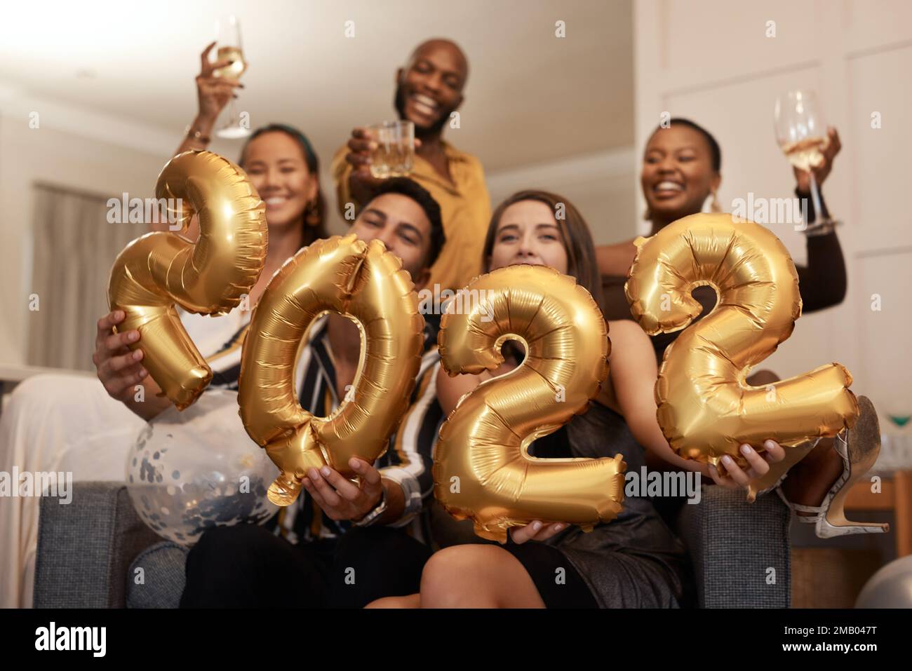 May the year be good to us. a diverse group of friends standing together and holding up 2022 balloons during a New Years party. Stock Photo