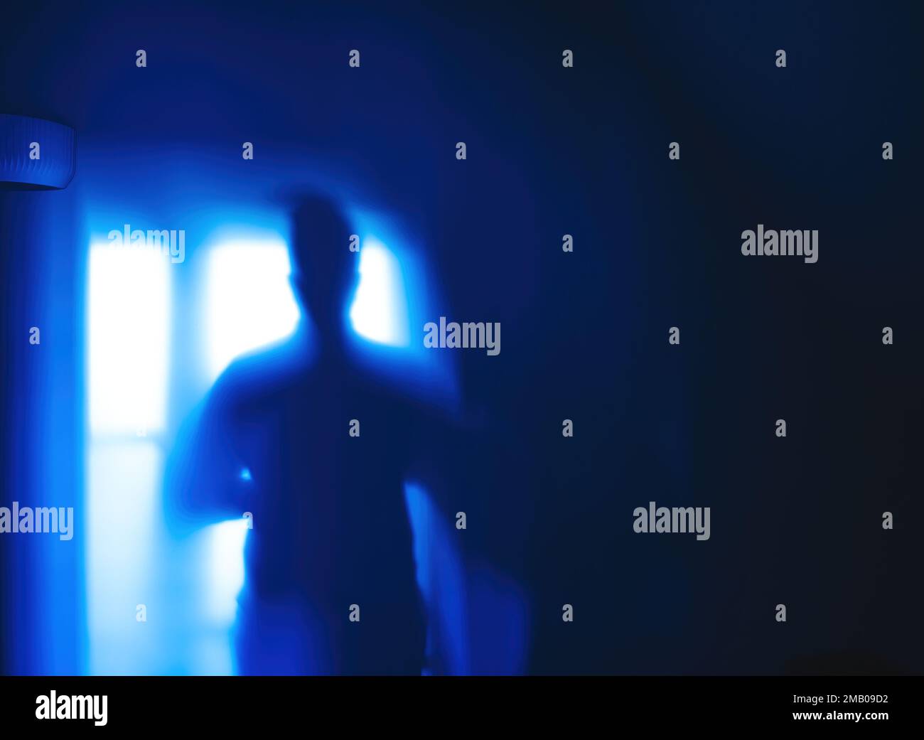 Silhouette shadow of a woman on a blue wall with white lamp in the left corner Stock Photo