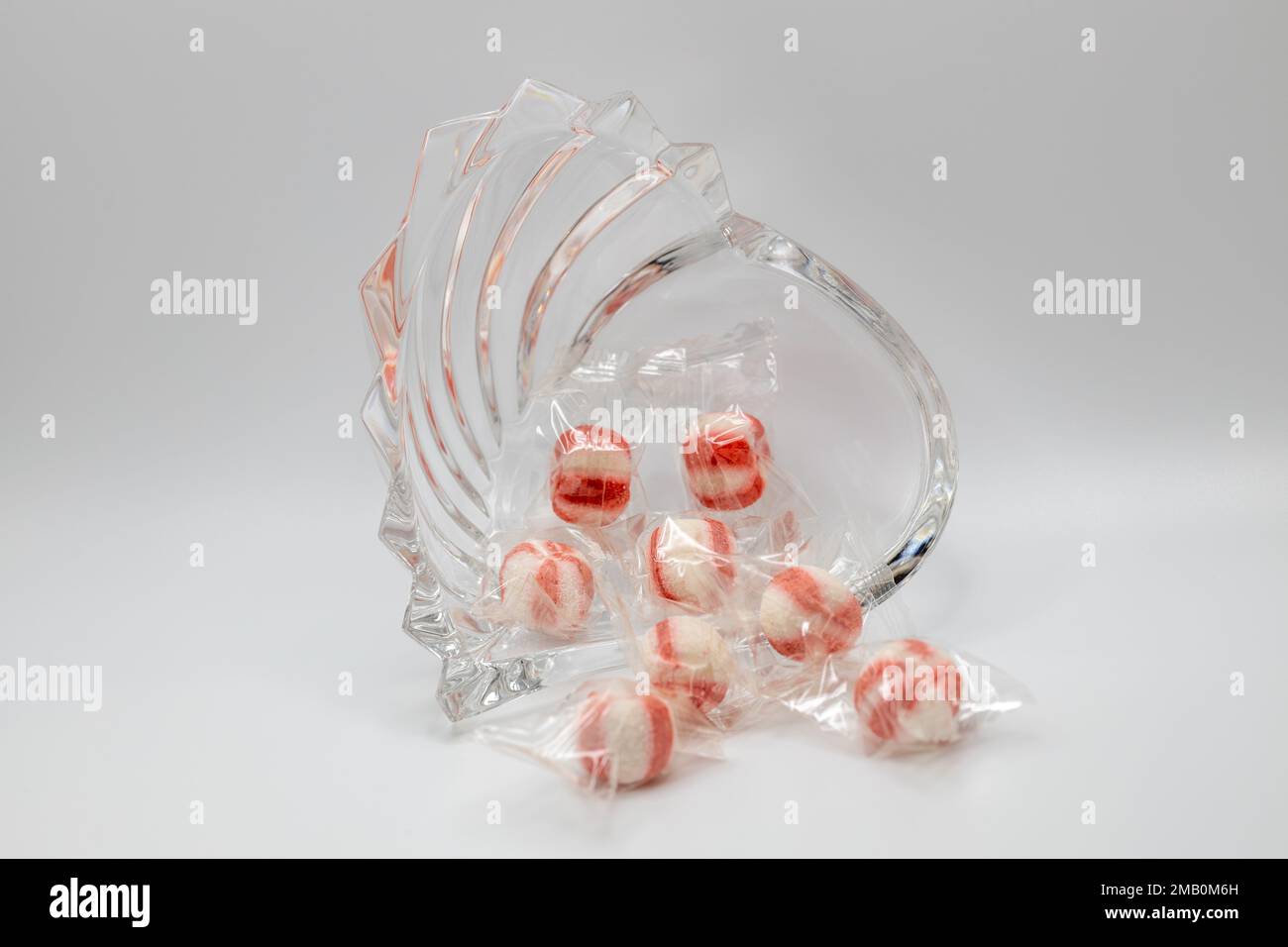 Macro view of a small beautiful heart-shaped crystal bowl containing hard puffed peppermint candies, on white background with copy space Stock Photo