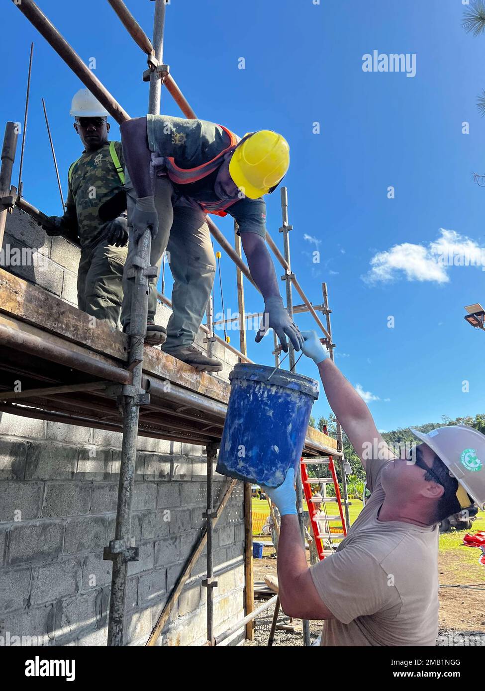 SAVUSAVU, Republic of Fiji (June 08, 2022) — Steelworker 3rd Class Bill Redmond, from Bakersfield, California, assigned to Naval Mobile Construction Battalion 3 (NMCB-3), passes a bucket of concrete to Sapper Epeli Naituku, assigned to the Republic of Fiji Military Forces, during a Pacific Partnership 2022 engineering project. Now in its 17th year, Pacific Partnership is the largest annual multinational humanitarian assistance and disaster relief preparedness mission conducted in the Indo-Pacific. Stock Photo