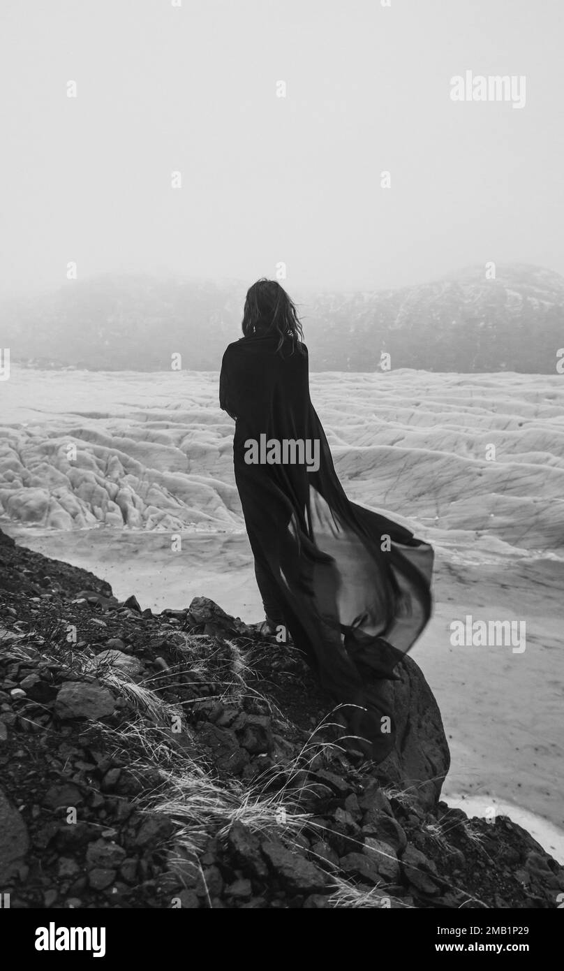 Lonely woman with fabric cape on rock monochrome scenic photography Stock Photo