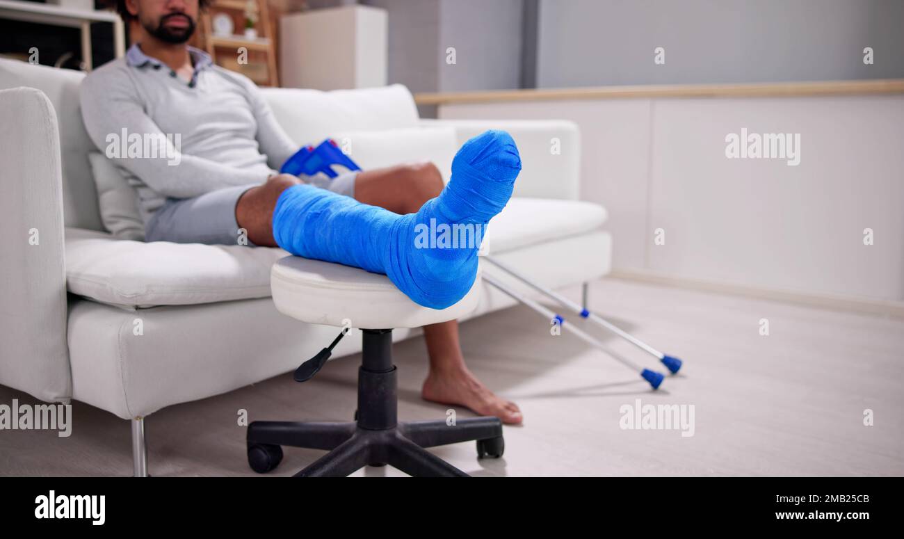 Young Man With Broken Leg Sitting On Sofa Stock Photo