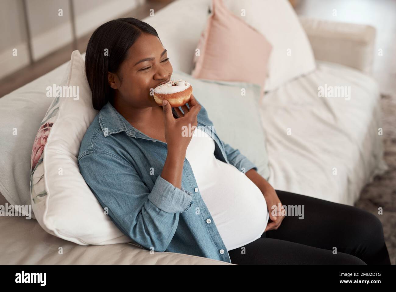 Giving in to her pregnancy cravings. a pregnant woman eating a donut at home. Stock Photo