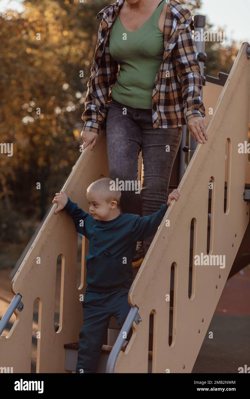 Little boy with Down syndrome going down the stairs on the playgroundk with his mother Stock Photo