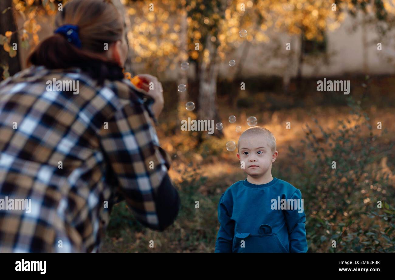 A boy, person with down syndrome walks in the park with his mother