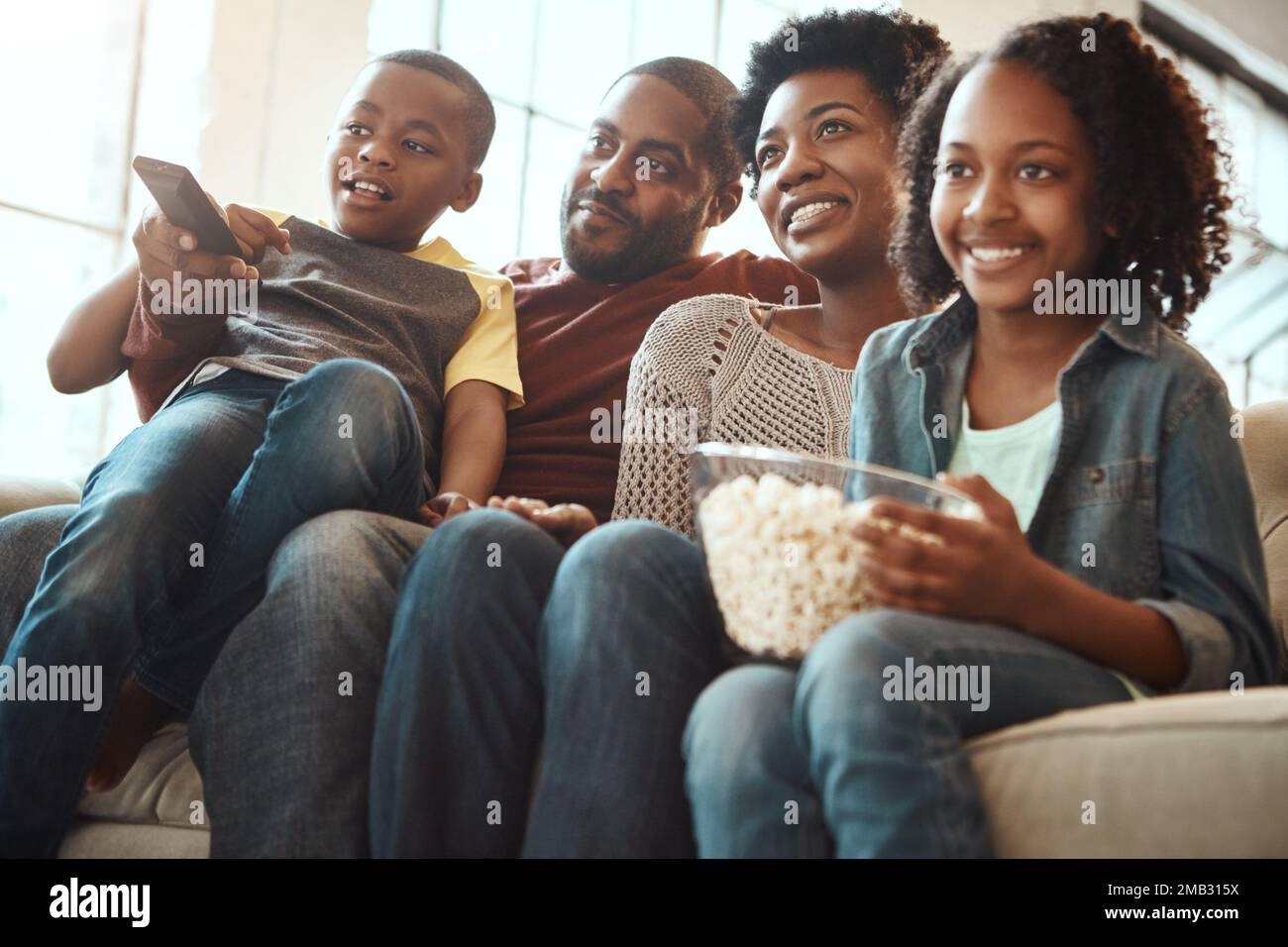 Black family watching tv on sofa for movie, film and cartoon together, bonding and quality time in living room. Popcorn, kids television show of Stock Photo