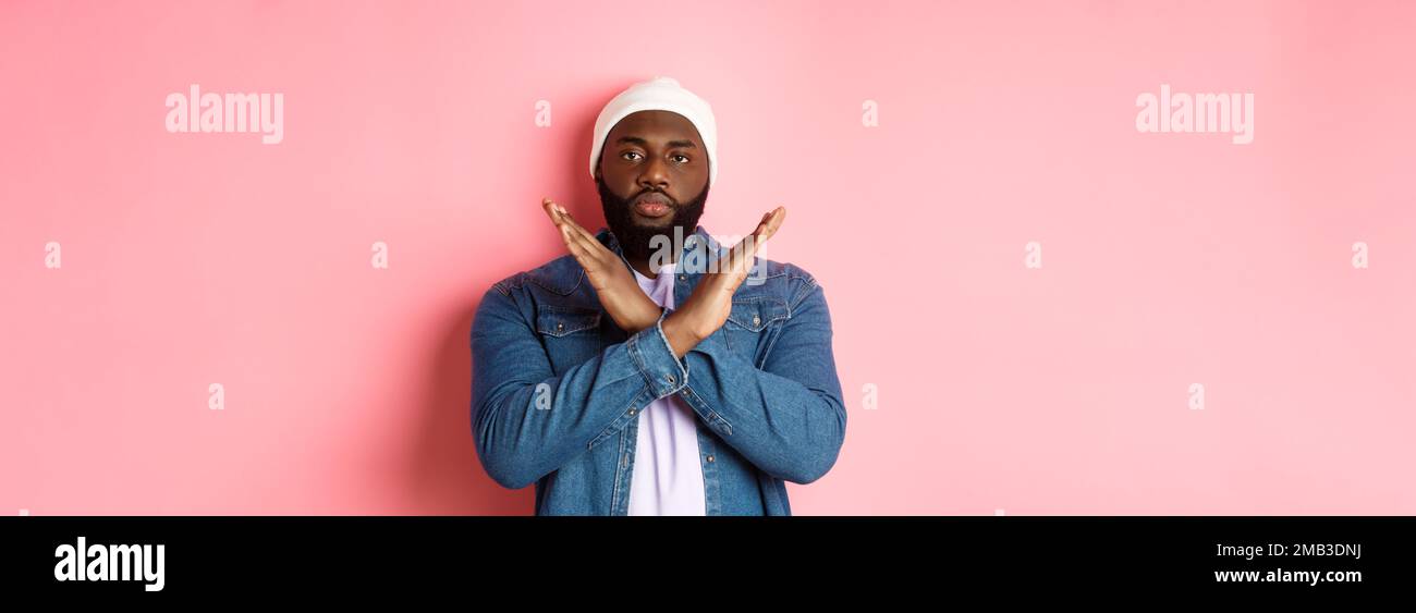 Serious african-american man saying no, showing cross to stop something bad, prohibit action, standing over pink background Stock Photo