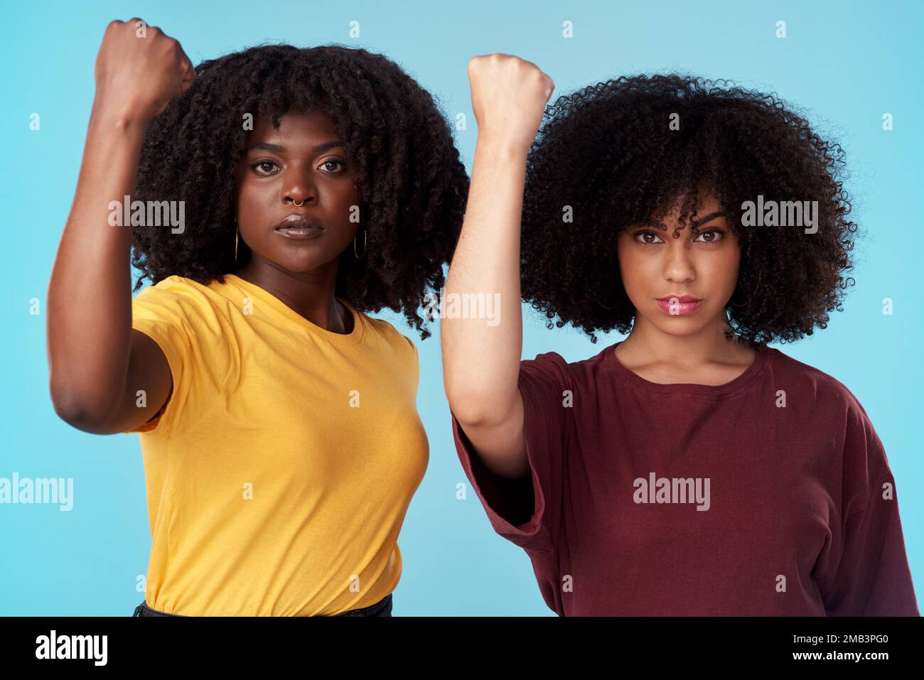 Together, we can overcome. Studio shot of two young women raising their fists in solidarity against a blue background. Stock Photo