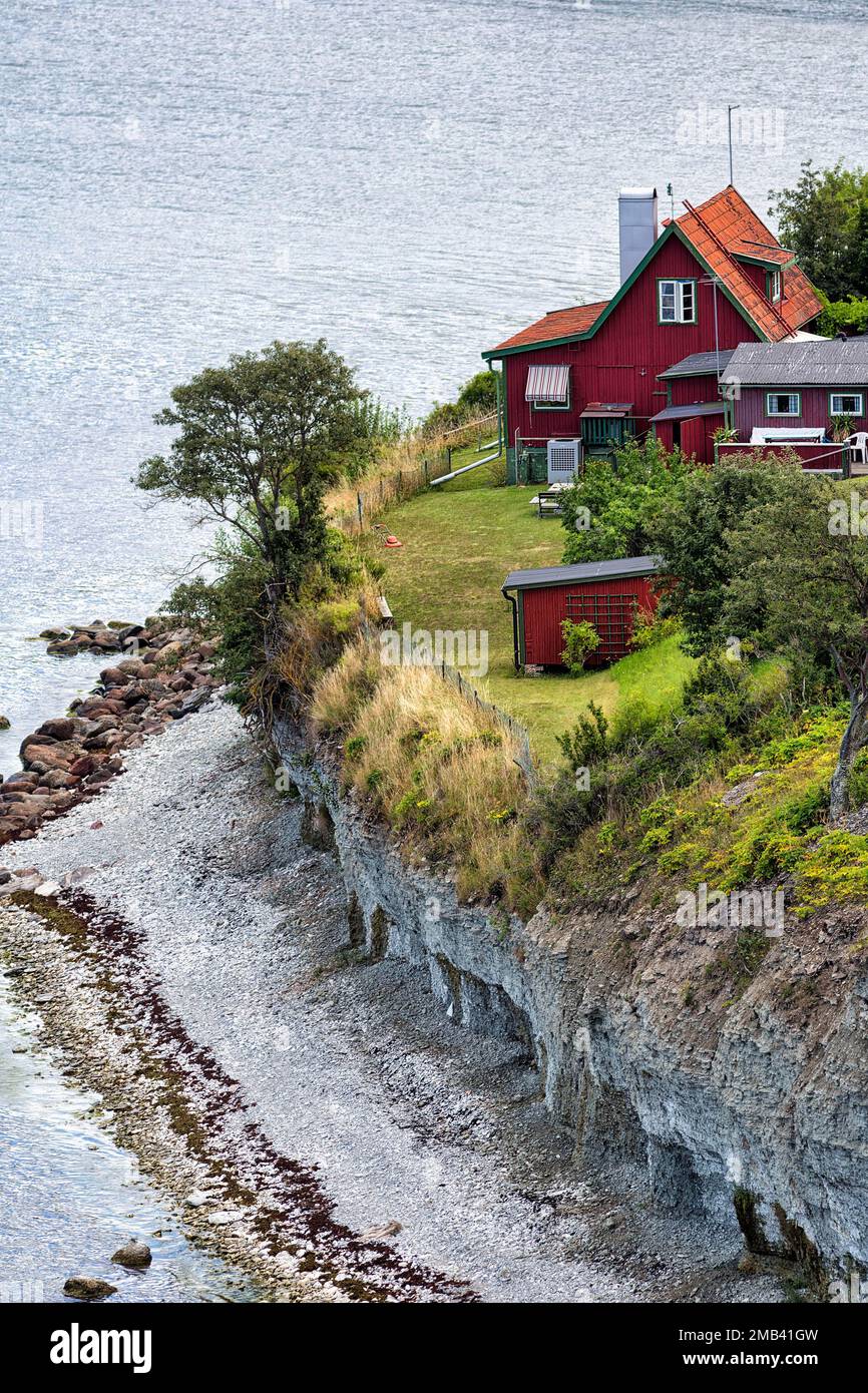 View from above on cliff coast, red Swedish house on edge, erosion, Hoegklint in summer, reef limestone, Visby, west coast, Gotland Island, Sweden Stock Photo
