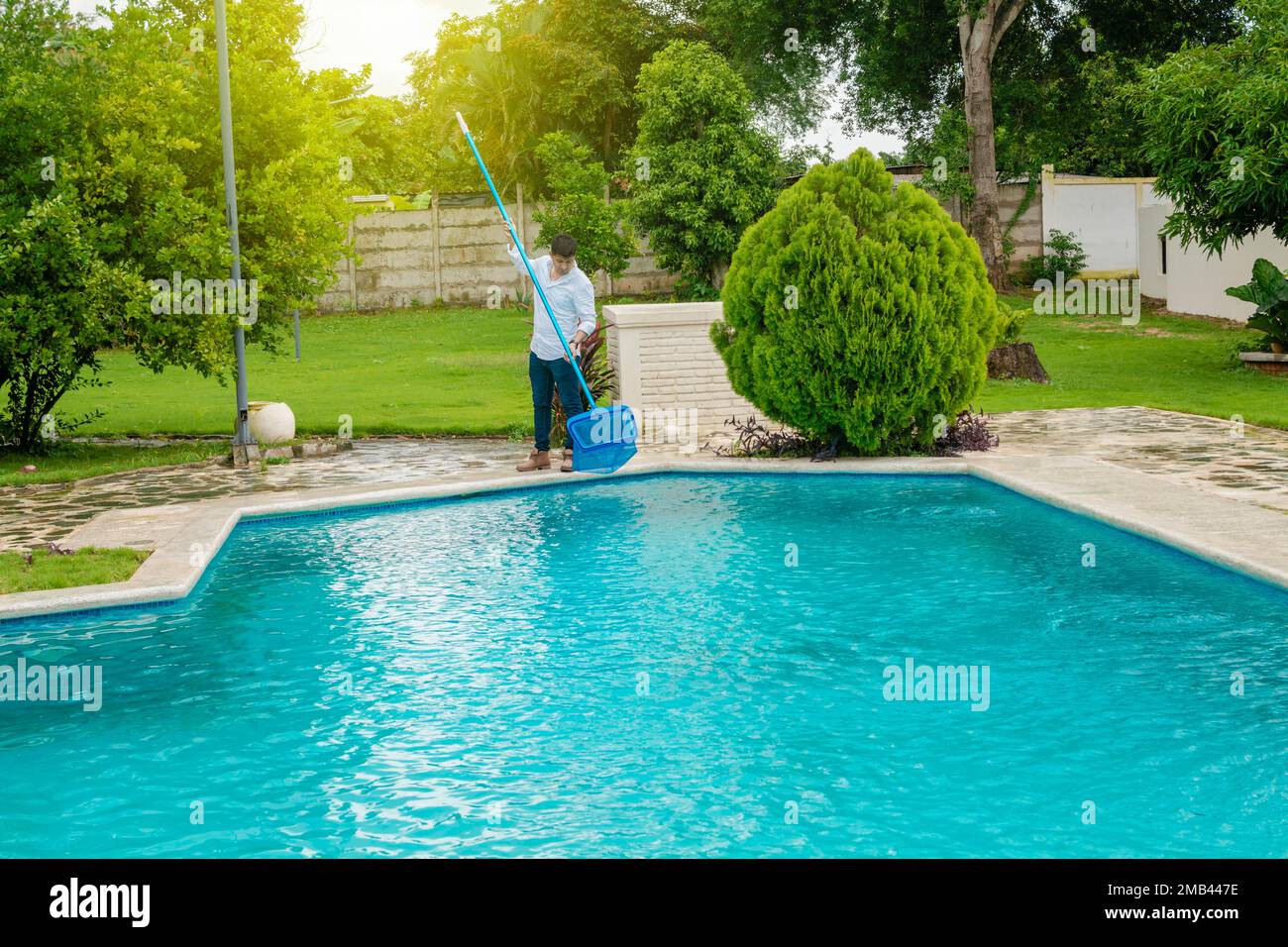 Man cleaning a swimming pool with skimmer, maintenance person cleaning