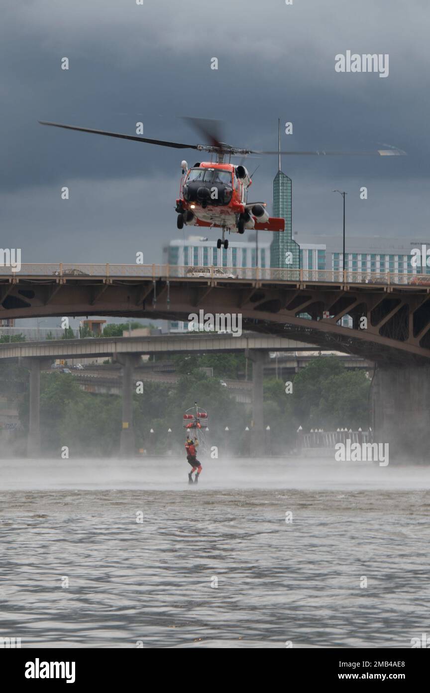 A Coast Guard aviation survival technician holds on to the basket  pulled out of the water by an MH-60 Jayhawk helicopter crew on the Willamette River in Portland, Oregon, June 11, 2022. The AST guided the basket deployment for the demonstration. Stock Photo