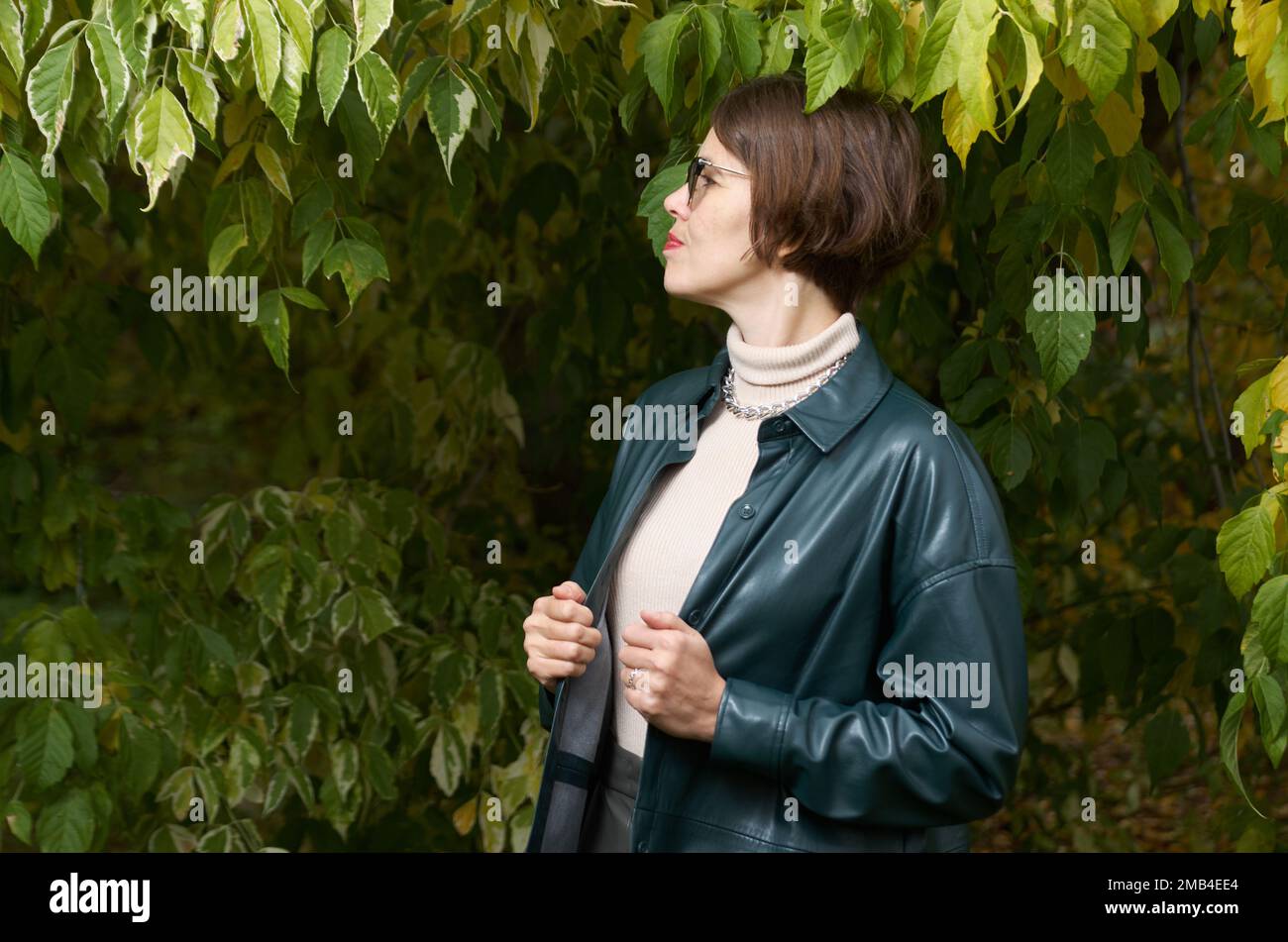 A woman in leather clothes stands in an autumn park Stock Photo